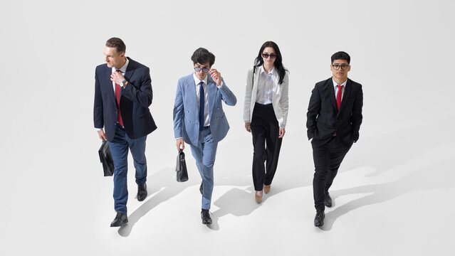 High angle view of young confident people dressed formal attire walking together with briefcases against white studio background. Concept of business, policy, confidence, communication, collaboration.