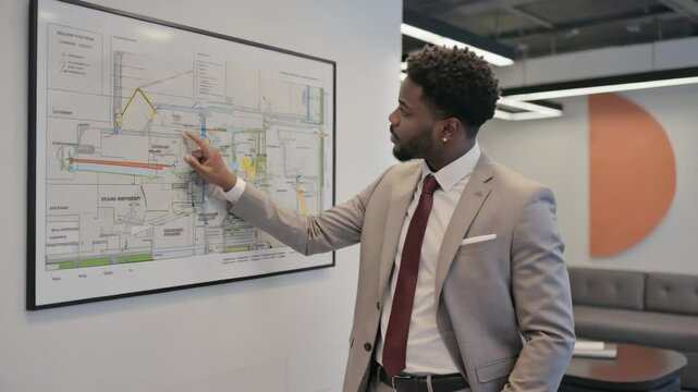 A confident engineer explains project routes on a wall chart with focused expression. Concept of smart city planning and technical expertise.