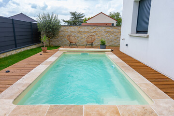 Vue d’ensemble d’une piscine aux rebords en carrelage, élégamment intégrée à une terrasse en bois dans un cadre extérieur moderne et apaisant.