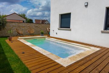 Piscine creusée avec rebords en carrelage, intégrée à une terrasse en bois moderne.