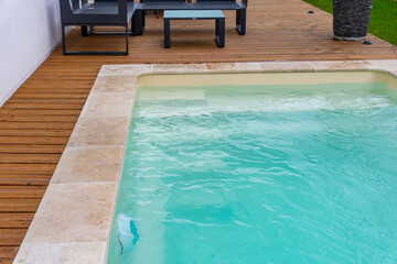 Vue latérale d’une piscine aux rebords en carrelage, intégrée à une terrasse en bois dans un environnement extérieur moderne.