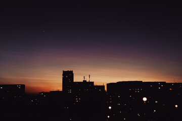 Colorful urban sunset with silhouettes of residential buildings and warm light glowing from the...