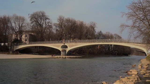 Munich, Germany. Scenic spring day in Munich historic center with locals strolling along the Isar River near Mariannenbruecke and St. Lukas Church under a clear blue sky. 