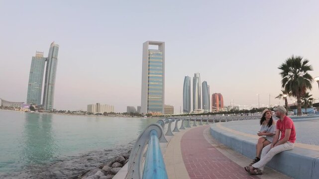Abu dhabi, UAE - 25th april, 2025: sunset timelapse couple visitors enjoy relaxed moment sit on bench enjoy sunset by Etihad Towers in Abu Dhabi, architecture with public space and modern city life