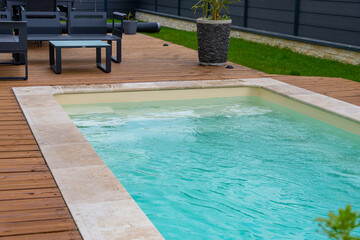 Vue latérale d’une piscine aux rebords en carrelage, intégrée à une terrasse en bois dans un environnement extérieur moderne.