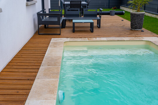 Vue lat&eacute;rale d&rsquo;une piscine aux rebords en carrelage, int&eacute;gr&eacute;e &agrave; une terrasse en bois dans un environnement ext&eacute;rieur moderne.