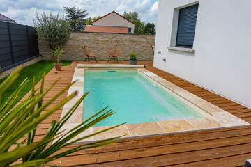 Piscine creusée avec rebords en carrelage, intégrée à une terrasse en bois moderne.