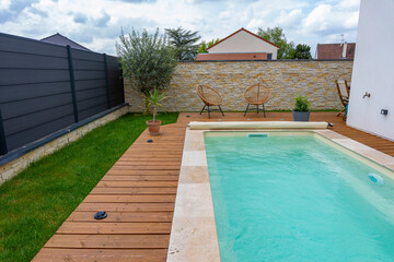 Vue du côté d'une piscine aux rebords en carrelage, installée sur une terrasse en bois, offrant une ambiance élégante et relaxante.