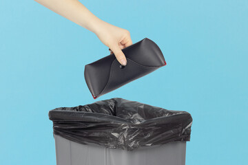 throwing glasses case into trash, outstretched hand with leather glasses case in front of trash can