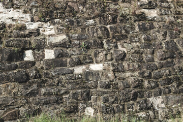 Detailed view of historic stone wall with moss and grass at the base in sunny daylight