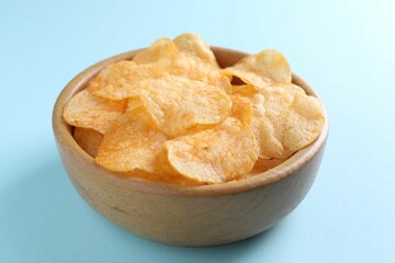 Tasty potato chips in bowl on light blue background, closeup