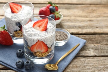 Delicious dessert with chia seeds, yogurt, granola, strawberries and blueberries on wooden table, closeup with space for text. Superfood