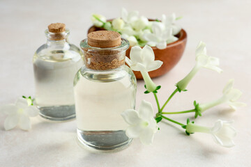 Bottles of essential oils and jasmine flowers on beige table, closeup