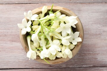 Beautiful jasmine flowers in bowl on wooden table, top view