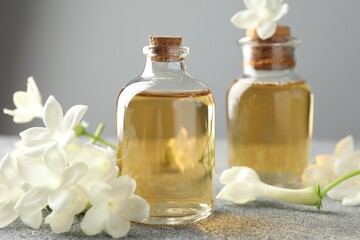 Bottles of essential oil and jasmine flowers on grey table, closeup