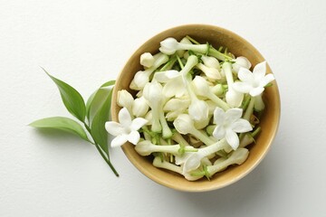 Beautiful jasmine flowers in bowl and green leaves on white table, flat lay