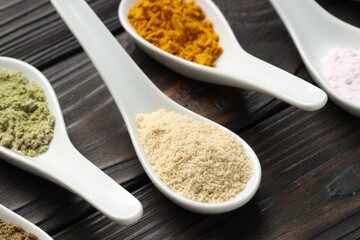Different superfood powders in spoons on wooden table, closeup