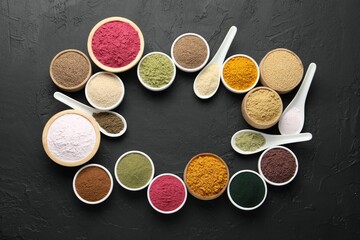 Frame of different superfood powders in bowls and spoons on dark textured table, flat lay. Space for text