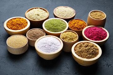 Different superfood powders in bowls on dark textured table