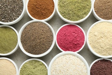 Different superfood powders in bowls on grey textured table, flat lay