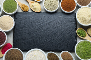 Different superfood powders and slate board on grey textured table, flat lay. Space for text