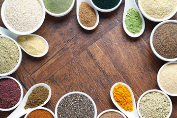 Frame of different superfood powders in bowls and spoons on wooden table, flat lay. Space for text