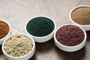 Different superfood powders in bowls on wooden table, closeup