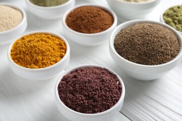 Different superfood powders in bowls on white wooden table, closeup