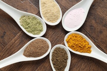 Different superfood powders in spoons on wooden table, flat lay