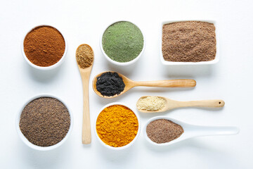 Different superfood powders in bowls and spoons on white background, flat lay