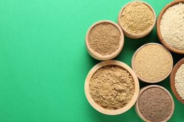 Different superfood powders in bowls on green background, flat lay. Space for text