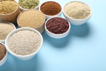 Different superfood powders in bowls on light blue background, closeup. Space for text