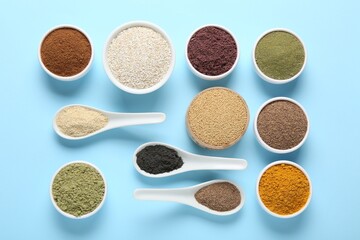 Different superfood powders in bowls and spoons on light blue background, flat lay