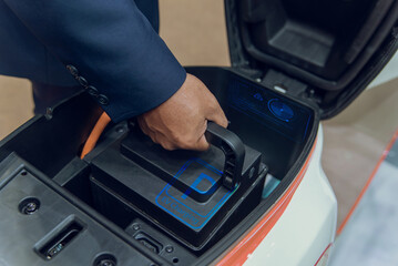 A person placing a removable electric scooter battery into the compartment, indicating EV charging and mobility solutions.