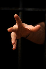 Man’s hand reaching through dark prison bars, grasping for freedom. Hand emerging from dark jail...