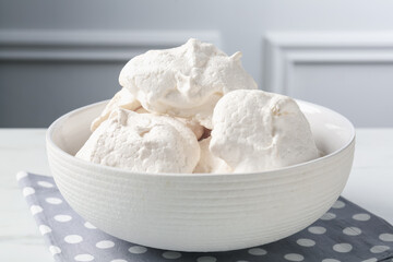 Delicious homemade meringue cookies in bowl on light table, closeup