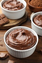 Tasty pudding in bowls and pieces of chocolate on wooden table, closeup