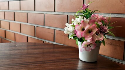Charming Artificial Flower Arrangement in White Pot on Wooden Table Near Brick Wall