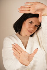 Happy dark haired woman got inspiration to imagine hot to take an interesting picture. Taking a picture with a gesture, smiling with pleasure. Dressed in casual clothes, isolated on beige background.
