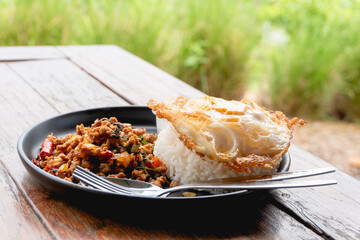 Stir-fried pork and basil leaves with rice and a fried egg served on white plate on wooden table...
