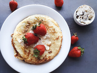 pancakes with cream, strawberries and cereal on white plate and gray background