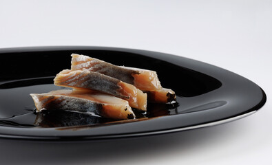 Several pieces of herring on a black plate. Herring fillet.