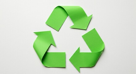 Obraz premium Close-up of a green recycling symbol made of paper on a white background, symbolizing environmental awareness and sustainability.
