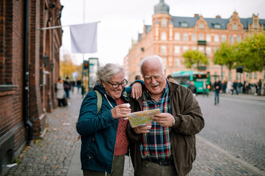 Senior couple laughing while reading map during city vacation