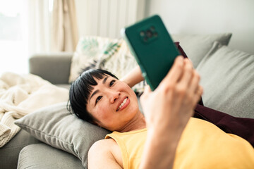 Smiling woman relaxing on couch having video call on smartphone