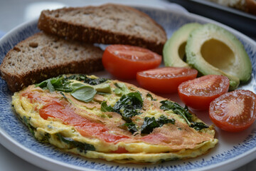 Omelet with greens and tomatoes served with whole grain bread and avocado, creating a healthy start to the day