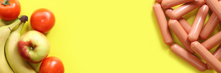 Products on a bright yellow background, top view. Fruits and vegetables lie opposite sausages. Space for text in the center of the photo. Food. Vegetarianism or meat-eating. Banner