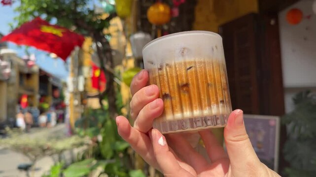 female hand holding a cup of salty coffee egg Vietnamese coffee on a background with a flag coffee shop travel on the street