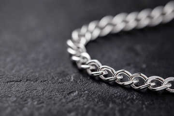 Closeup of a shining silver chain on a textured dark background. Elegant silver chain captured in a detailed closeup with bright lighting on plain blue background.