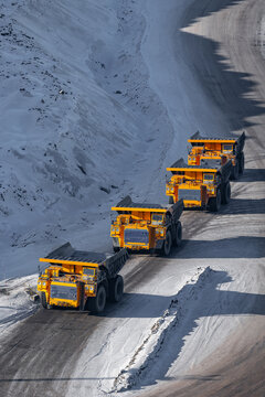 Quarry dump trucks queue for refueling in open pit coal mining, winter landscape